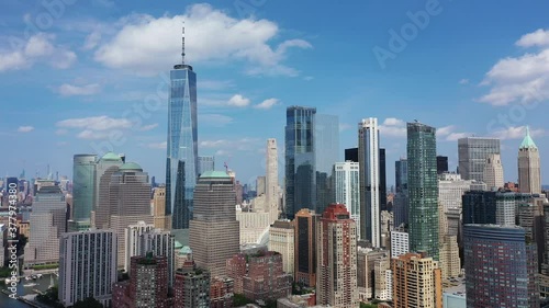 An aerial view over lower Manhattan. The drone trucks and pans right, orbiting the buildings. The freedom tower is the main attraction on this beautiful day with blue skies and a few clouds.