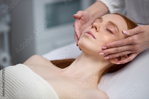 caucasian professional cosmetologist applying special cream while doing anti age procedure for young redhead female