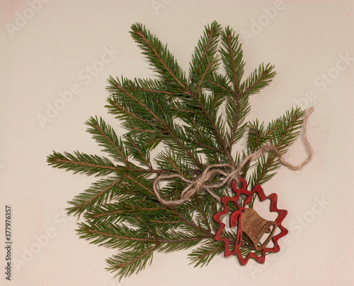 Fir tree branches and decorative handmade wooden bell on light yellow background. Christmas hamdmade gift concept. photo