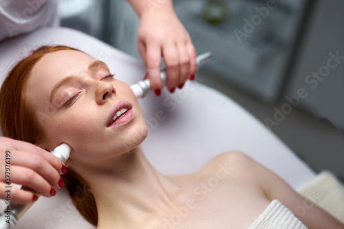 facial skin rejuvenation by microcurrent therapy in cosmetology salon, using special device to perform a facial rejuvenation procedure for attractive caucasian young female