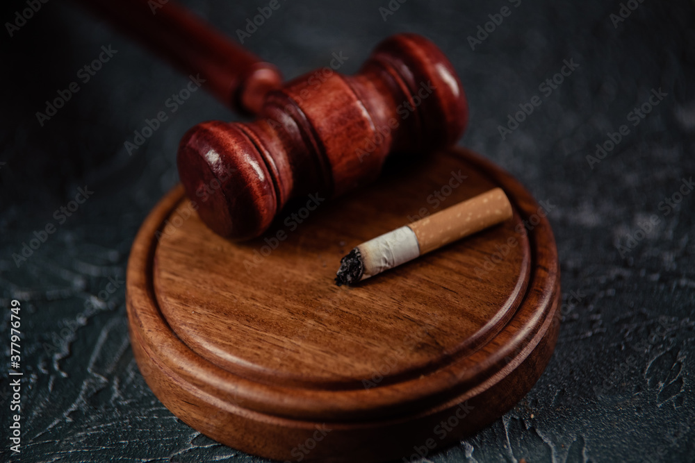 Wooden judge gavel and cigarette on grey table. Tobacco law concept.