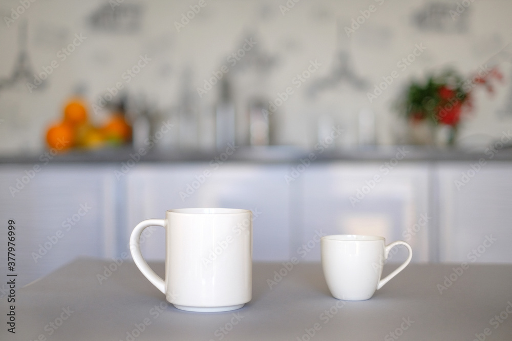 Two white cups of coffee on white kitchen defocused background