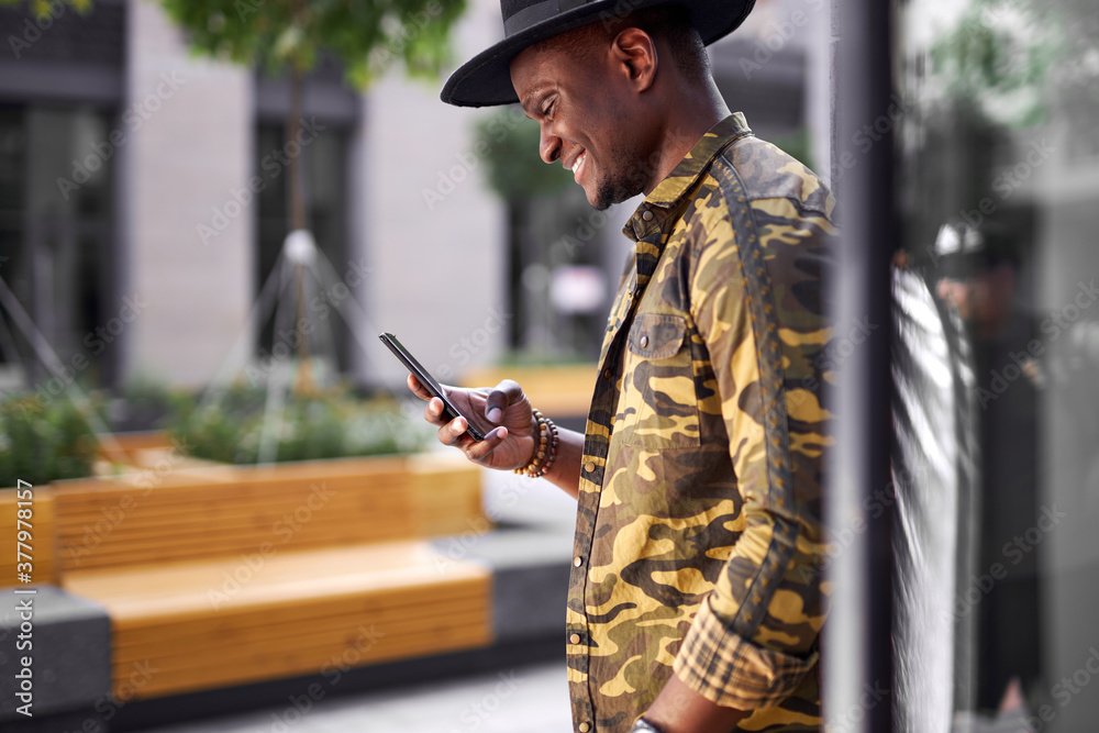 handsome dark-skinned man chatting with friend outdoors, young male look at smartphone and smile