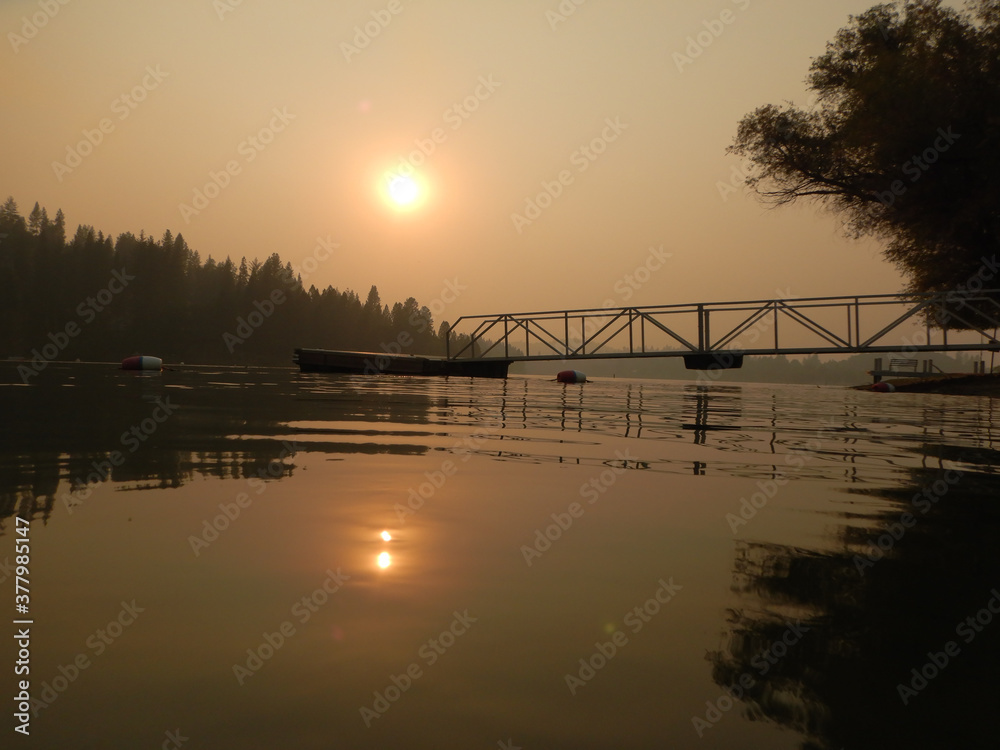 Smokey sunset view over the lake with a dock, trees, and the sun reflected in the water