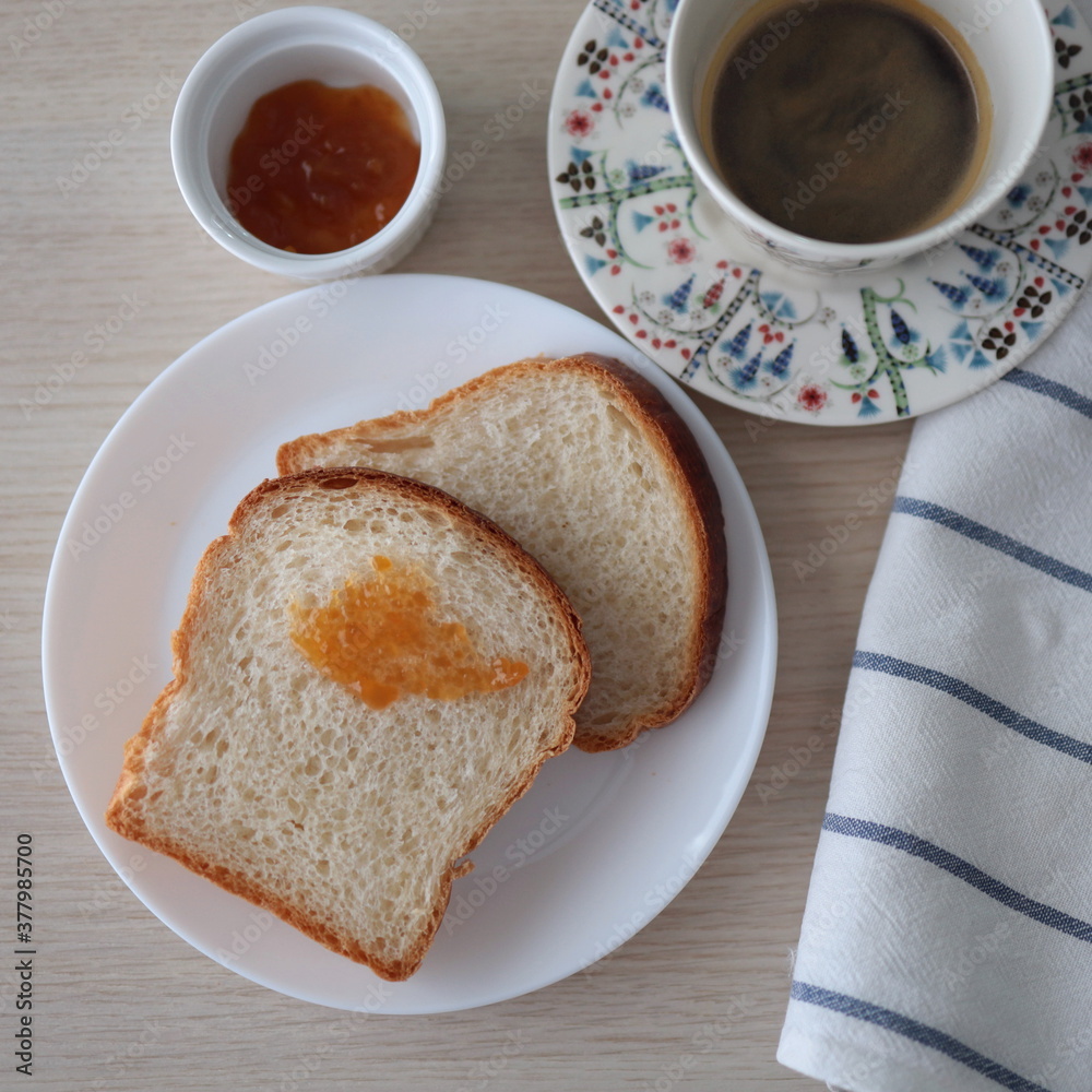 Morning toasts with apricot jam on white plates and served with a cup of black coffee. Wooden background and top view. Morning toasts with apricot jam on white plates and served with a cup of black coffee. Wooden background and top view.