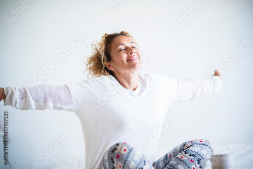 Happy beautiful woman wake up in the morning at home or hotel room enjoying the life with a smile and opening arms to stretch and start the new day - concept of waking up with joy
