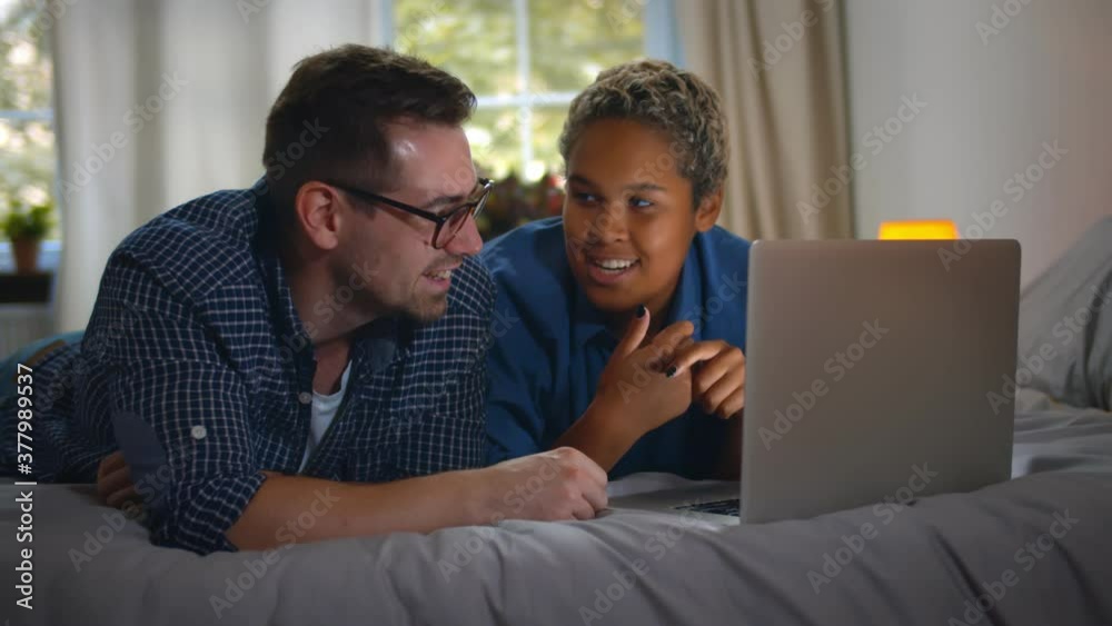 Happy diverse couple lying on bed while using laptop Happy diverse couple lying on bed while using laptop