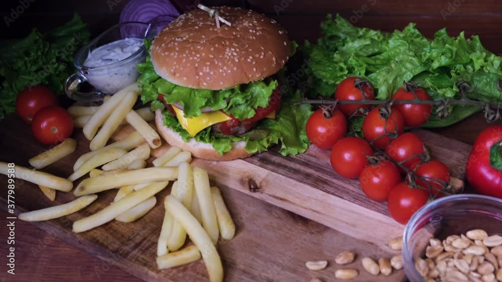 A wooden table with beer, burger and fries. The hand raises the glass of beer and returns it empty. Fast food and beer concept. A wooden table with beer, burger and fries. The hand raises the glass of beer and returns it empty. Fast food and beer concept.
