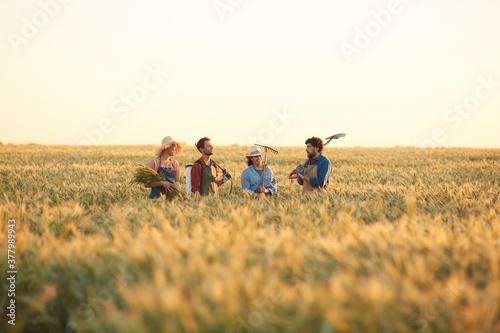 Wide angle view at workers holding tools while walking across golden field in sunset light, copy space