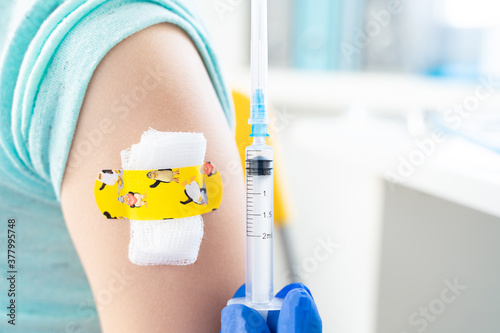 Vaccination of little girl in doctor's office. Kids funny adhesive plaster,gauze napkin.Syringe with vaccine for covid-19 coronavirus,flu,infectious diseases. njection.Clinical trials for human,child photo