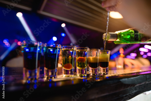 Bright cocktails - shots at the bar. Colorful footage in a nightclub. Alcoholic drink of different colors. Nightlife scene. Shots at the bar table. Several glasses of alcohol 