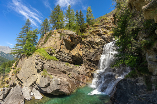 une cascade en montagne avec son eau verte et des sapins