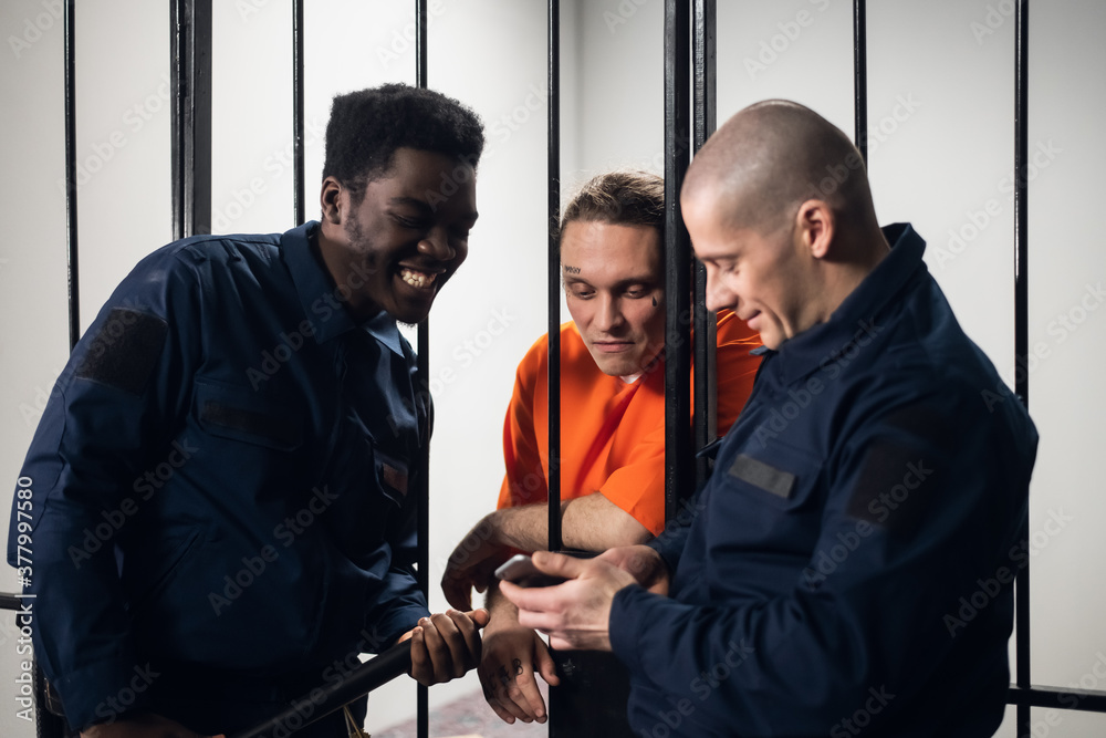 The prison guards make friends with the prisoner and watch funny videos on their smartphone together The prison guards make friends with the prisoner and watch funny videos on their smartphone together