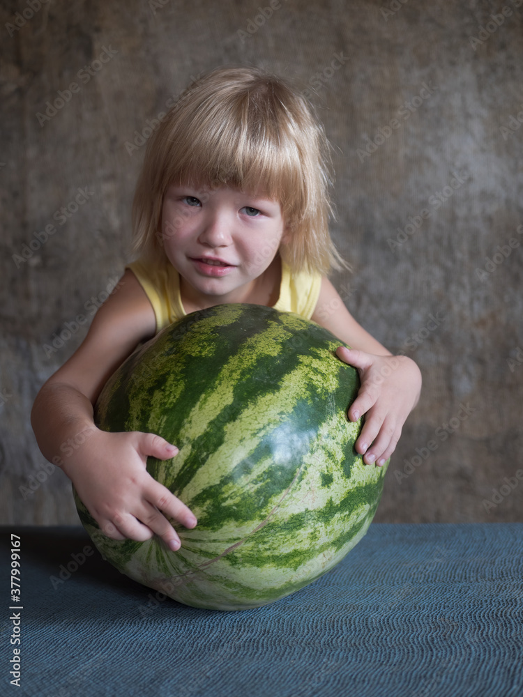 Funny blond boy hugs big watermelon lying on table with his hands Funny blond boy hugs big watermelon lying on table with his hands