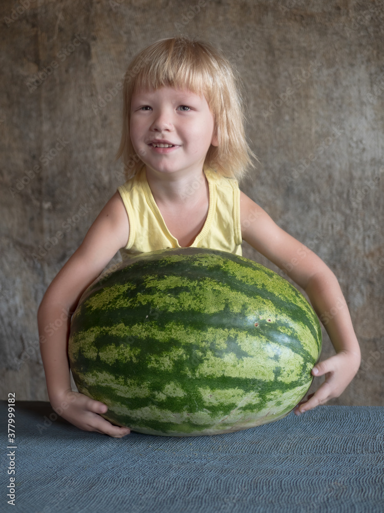 Fototapeta premium Funny blond boy hugs big watermelon lying on table with his hands