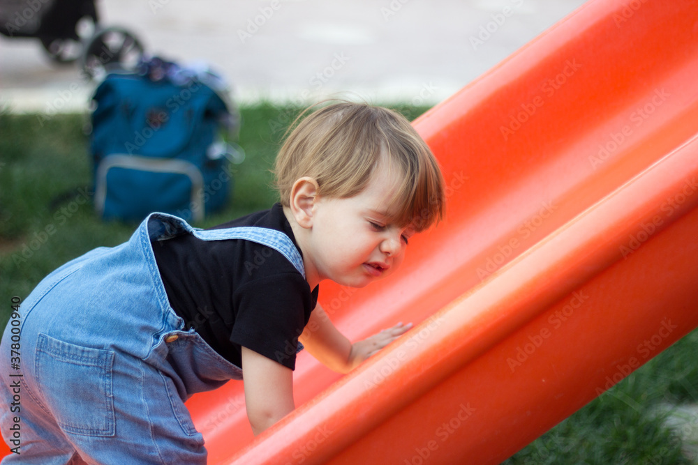 Obraz premium a baby trying hard to climb the slide in a park 
