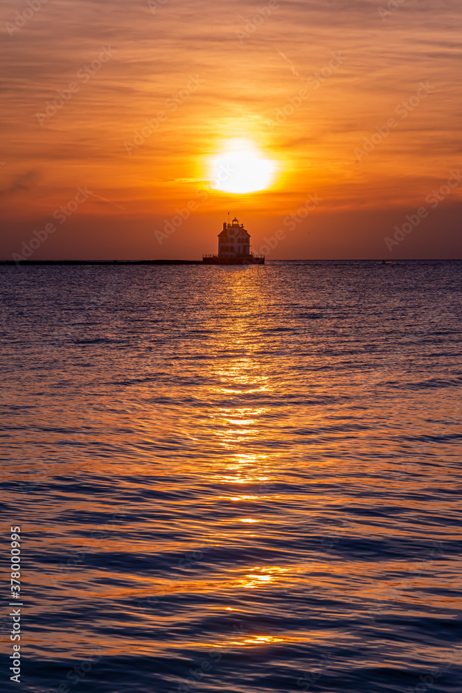 Lighthouse in the middle of calm water in bay with orange sunset