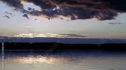 Summer sunset over the lake, dark clouds on the horizon. 