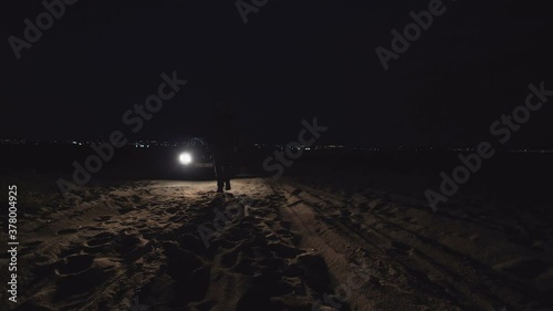 Silhouette Of Man IRun Away on Beach  In Front Of Car Headlights photo