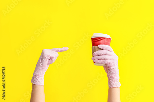 Hands in protective gloves and with cup of coffee on color background