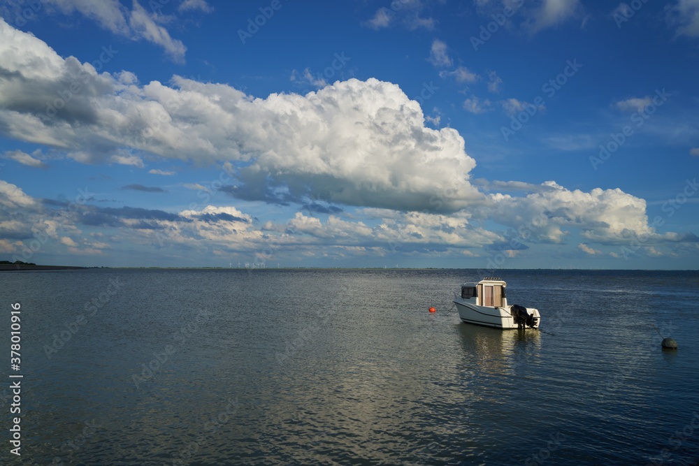 small white motor boat is lying in the water of the bay Jadebusen (Germany) under vivid blue sky with scenic white clouds