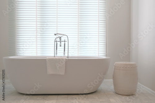 Minimalist luxury Bathtub with traditional faucets in front of closed venetian blinds photo