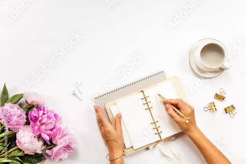 Well-groomed woman hands is writing in diary with stationery supplies set onside and peonies bouquet photo