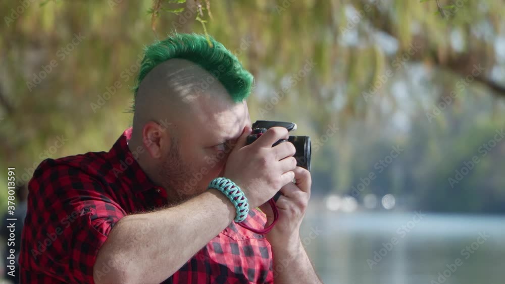 An alternative man with a green mohawk taking a photo with his camera at park