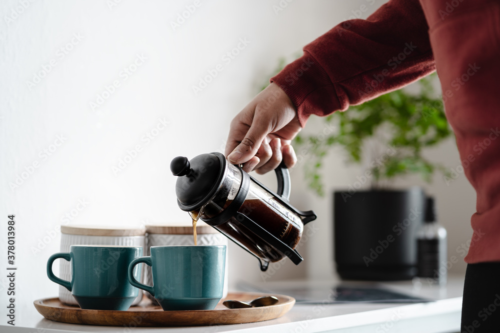 Woman pouring coffee in two coffee cups at morning