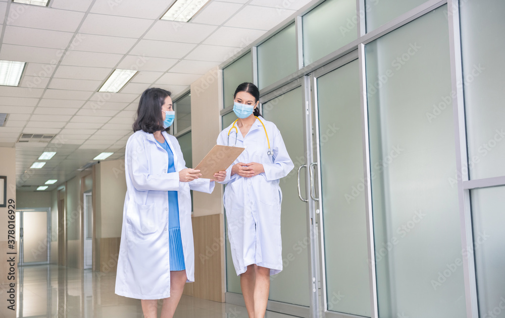 Two woman doctor with mask talking  in hospital corridor, health care.  female doctors examining a file in a bright office. people teamwork healthy and medicine concept