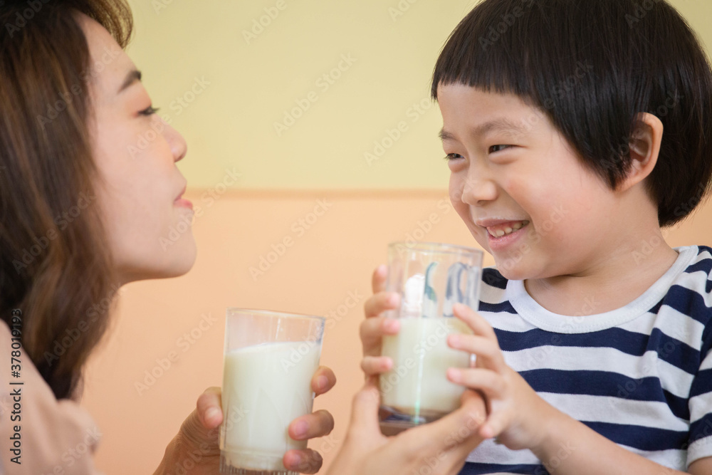 Woman is trying to encourage a smiling boy to drink a glass of milk together. Focused on a boy's face. Woman is trying to encourage a smiling boy to drink a glass of milk together. Focused on a boy's face.