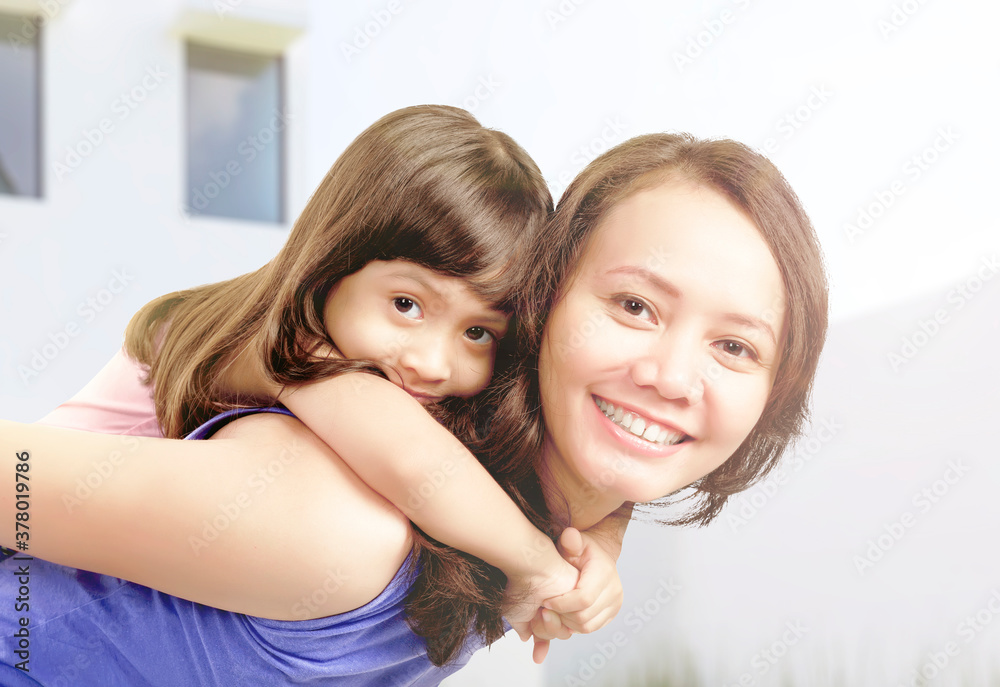 Asian mother carrying her little girl on her back with a smile on his face