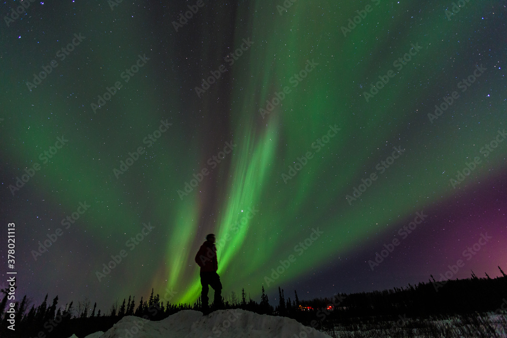Silhouette man standing on mound under northern lights Alakska. Auroras display dynamic patterns of brilliant lights that appear as curtains, rays, spirals, or dynamic flickers covering the entire sky