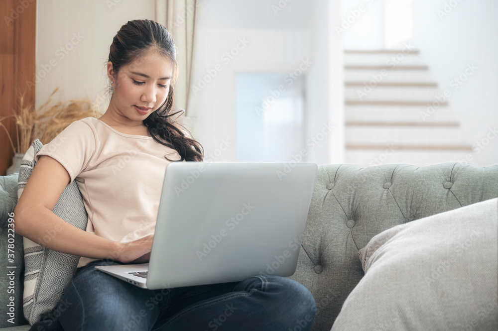 Young asian woman using laptop while sitting on sofa in living room at home. Young asian woman using laptop while sitting on sofa in living room at home.