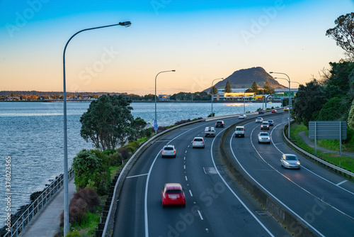 Cars in long exposure  blurred in motion travelling along Takitimu Drive with landmak Mount Maunganui in distance at sunrise. photo