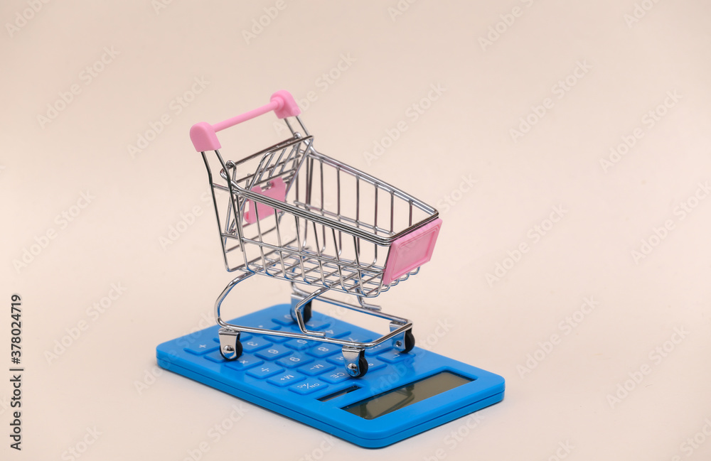 Market cost. Mini shopping trolley with calculator on beige background Market cost. Mini shopping trolley with calculator on beige background