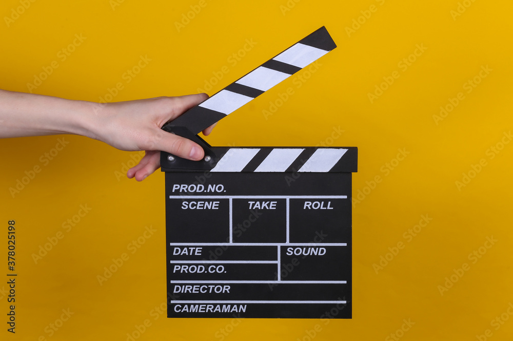 Hand holding film clapper board on yellow background. Cinema industry, entertainment.