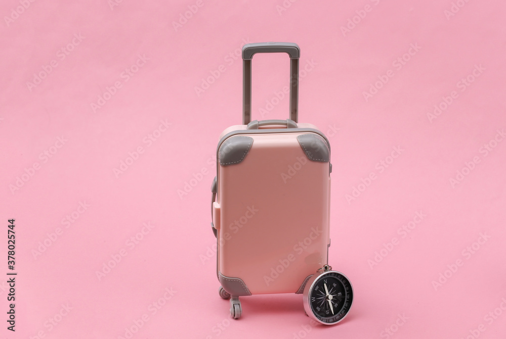 Travel or trip concept. Mini plastic travel suitcase and compass on pink background. Minimal style Travel or trip concept. Mini plastic travel suitcase and compass on pink background. Minimal style