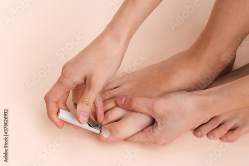 Woman cuts toenails with nail clippers on beige background. Self care concept