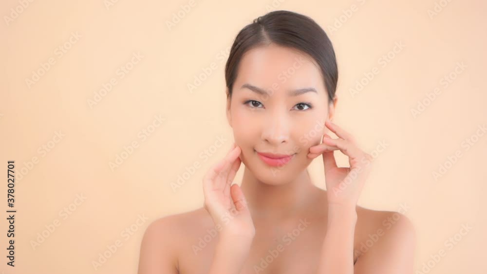 Attractive young Asian model with soft smooth skin runs fingers over her face with eyes closed then looks into camera. Cosmetics or skin care advertising concept with copy space left side. Attractive young Asian model with soft smooth skin runs fingers over her face with eyes closed then looks into camera. Cosmetics or skin care advertising concept with copy space left side.