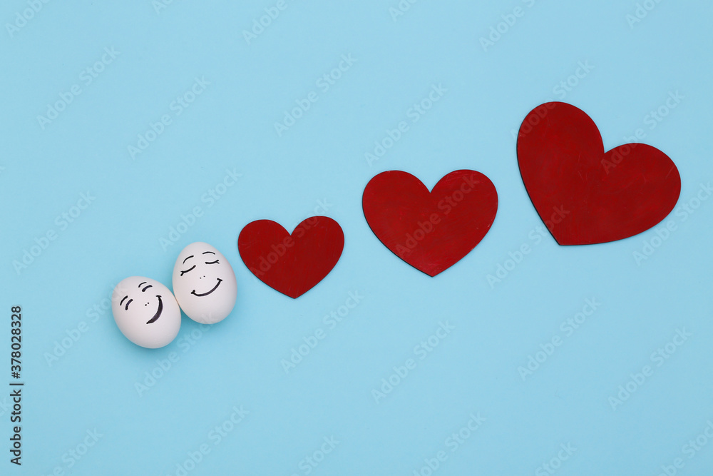 Happy loving couple of chicken eggs faces with hearts on blue background