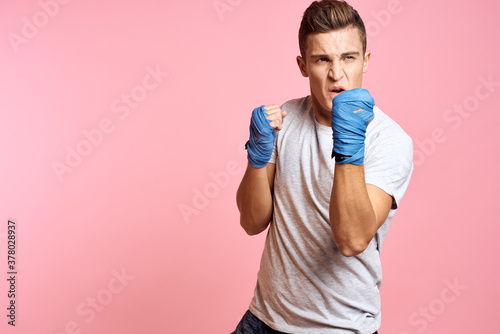 Guy in blue gloves on a pink background are boxing in a white t-shirt cropped view