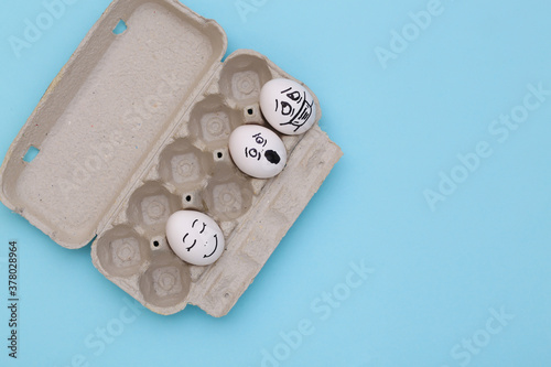 Covid -19 pandemic. Eggs tray with eggs by faces on a blue background. top view