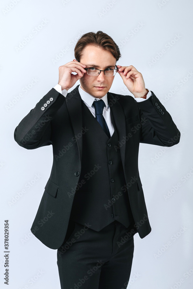 A man in a black suit adjusts his glasses. Light background A man in a black suit adjusts his glasses. Light background