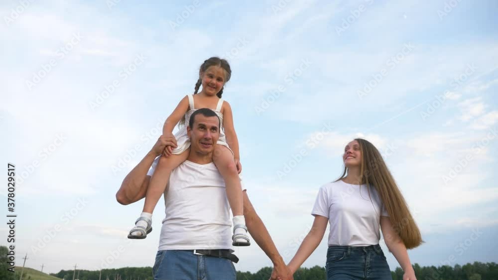 Happy young family spend time together. Father mother and daughter are walking on the lawn. Family in the Park for a walk. A caring father holds the baby on his shoulders. Happy young family spend time together. Father mother and daughter are walking on the lawn. Family in the Park for a walk. A caring father holds the baby on his shoulders.