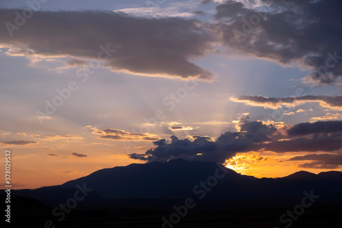 Beautiful golden sunset with sun beams, cloudy sky and mountains silhouettes, colorful nature background. Golden hour. Outdoor landscape. Adventure travel. Scenic view. Mountains background.