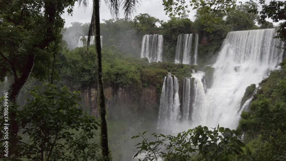 Impressive panoramic scene of UNESCO Iguazu falls of fresh white powerful raging water cascading over rocky cliff edge and pounding rocks below creating mist, Brazil, handheld pan right Impressive panoramic scene of UNESCO Iguazu falls of fresh white powerful raging water cascading over rocky cliff edge and pounding rocks below creating mist, Brazil, handheld pan right