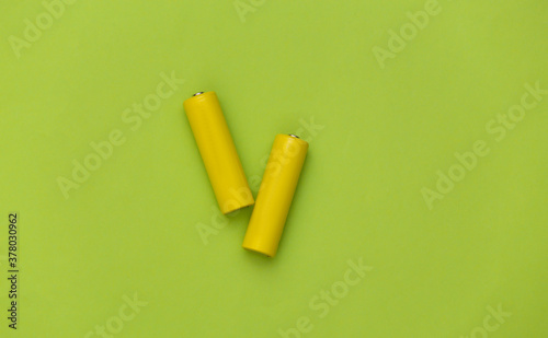 Two yellow AA battery on green pastel background. Top view