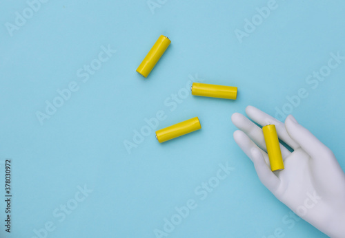 White mannequin hand holds AA type batteries on a blue background. Top view