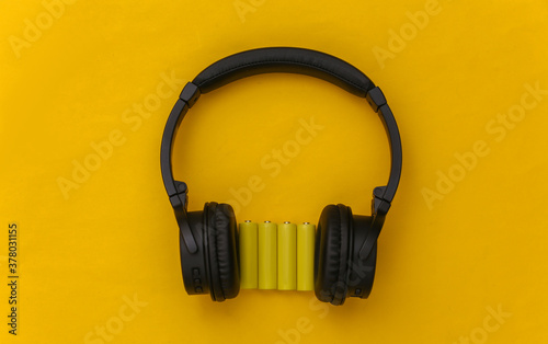 Wireless stereo headphones and four yellow AA batteries on yellow background. Top view